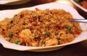 Shrimp fried rice on white serving plate with spoon on table.