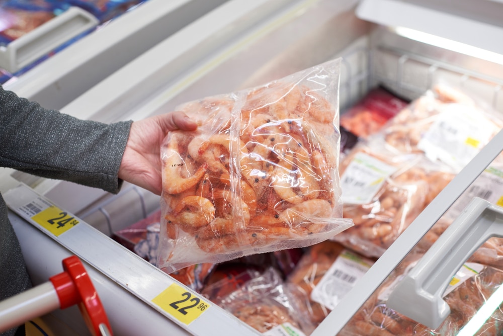 A person shopping for frozen shrimp at a grocery store.