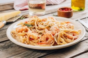 A plate of shrimp pasta with drinks and garnishing.