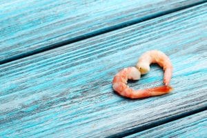 A pair of boiled shrimp forming a heart on a blue wooden table.