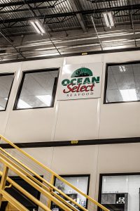 The Ocean Select Seafood logo on a wall overlooking the company's facility floor.