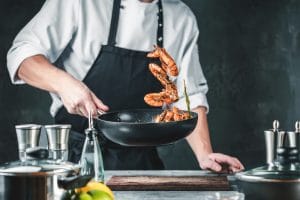 A chef cooking shrimp in a pan.