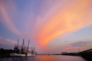 A shrimp boat in water under a sunset sky.