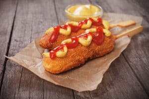 Two shrimp corn dogs with ketchup and mustard on wax paper.